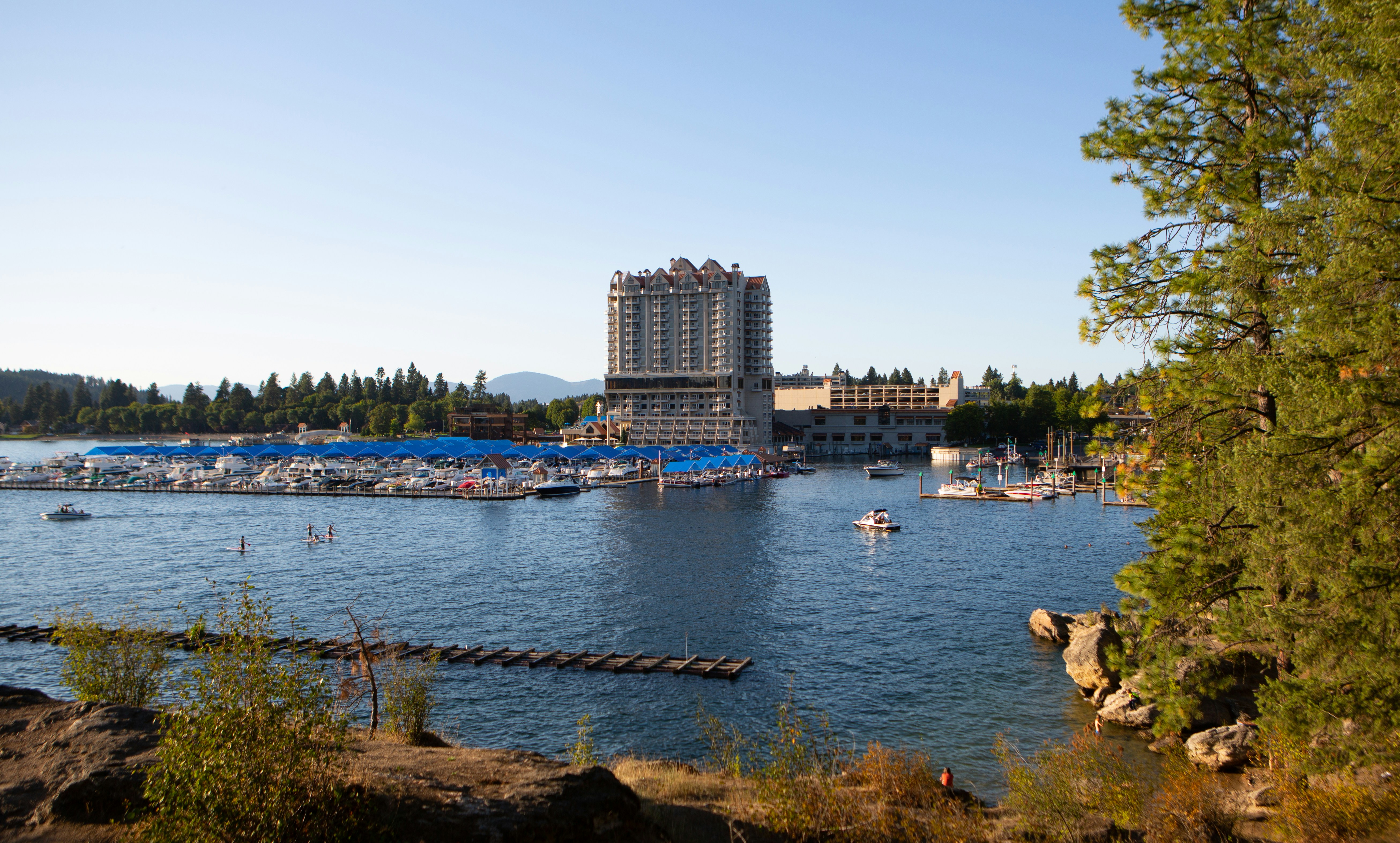 Coeur d’Alene’s lakefront marina on a clear afternoon, pines along the near shore.